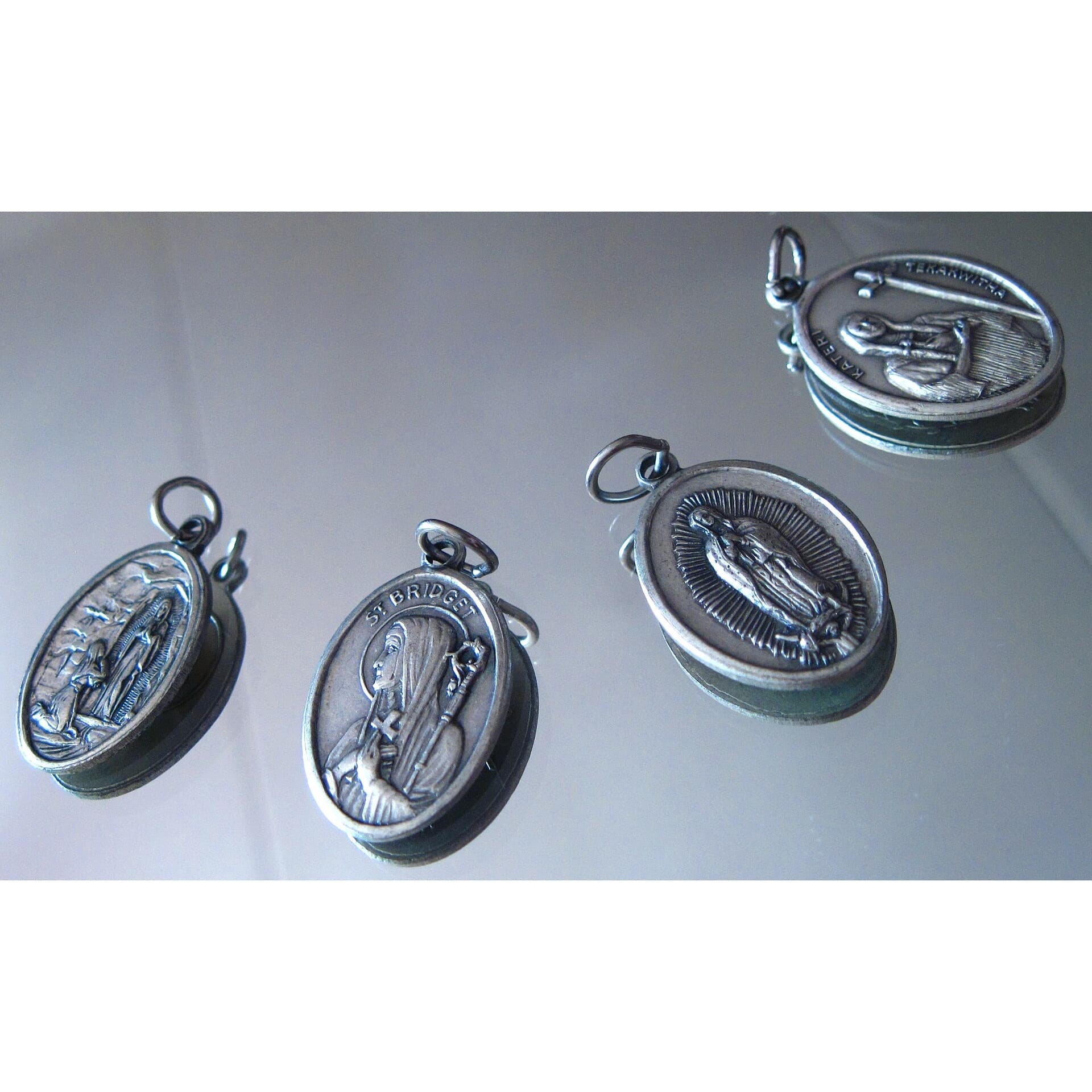 Four silver devotional medals laid out on a reflective surface