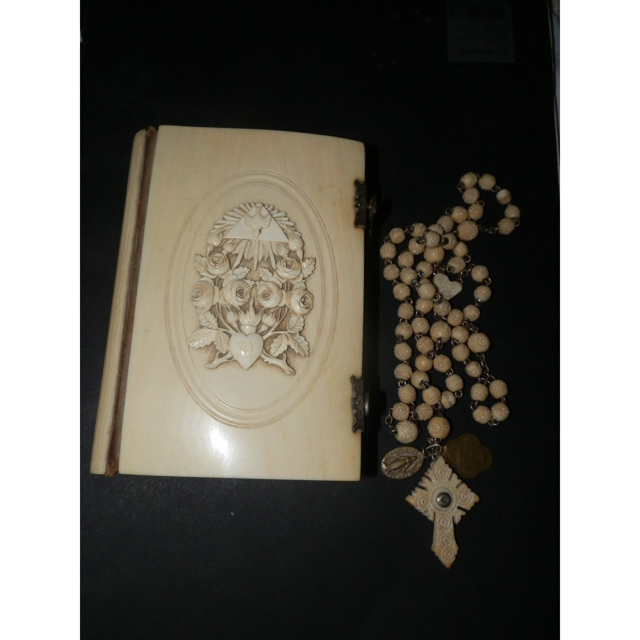 An ornately carved rosary with crucifix laid beside a devotional book