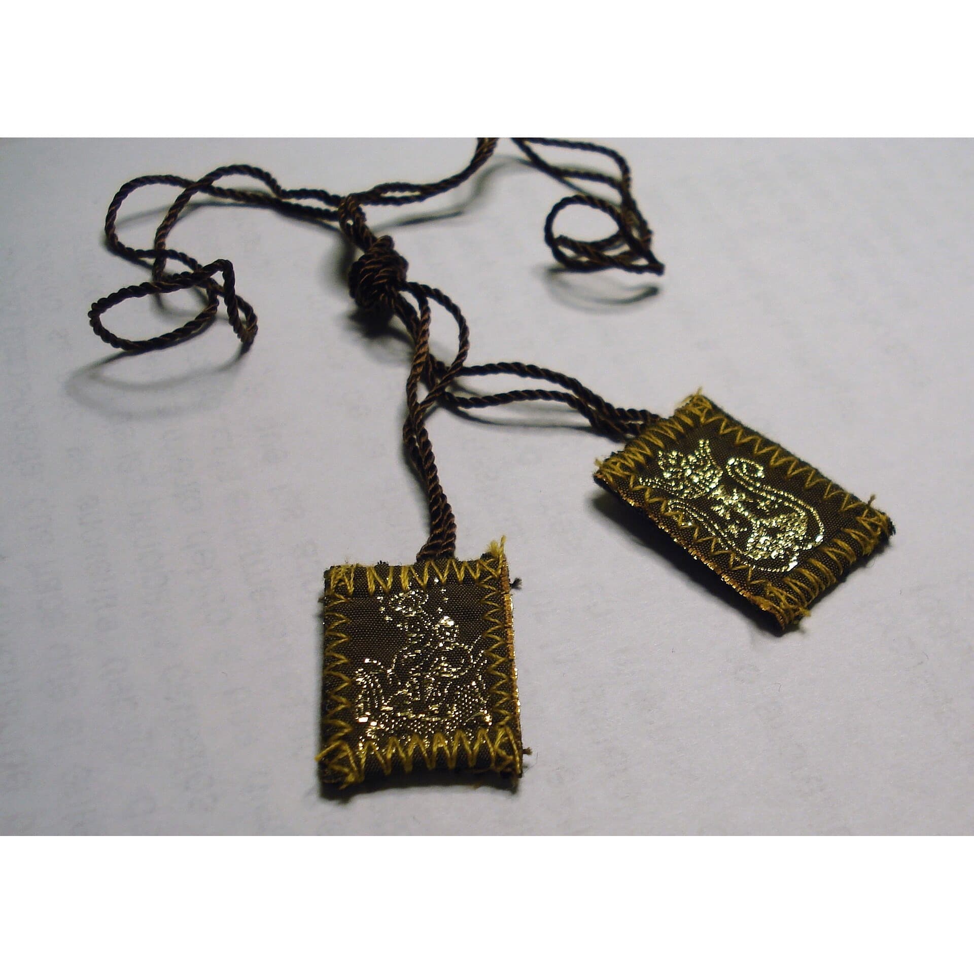 Brown embroidered scapular with braided cord on a plain background